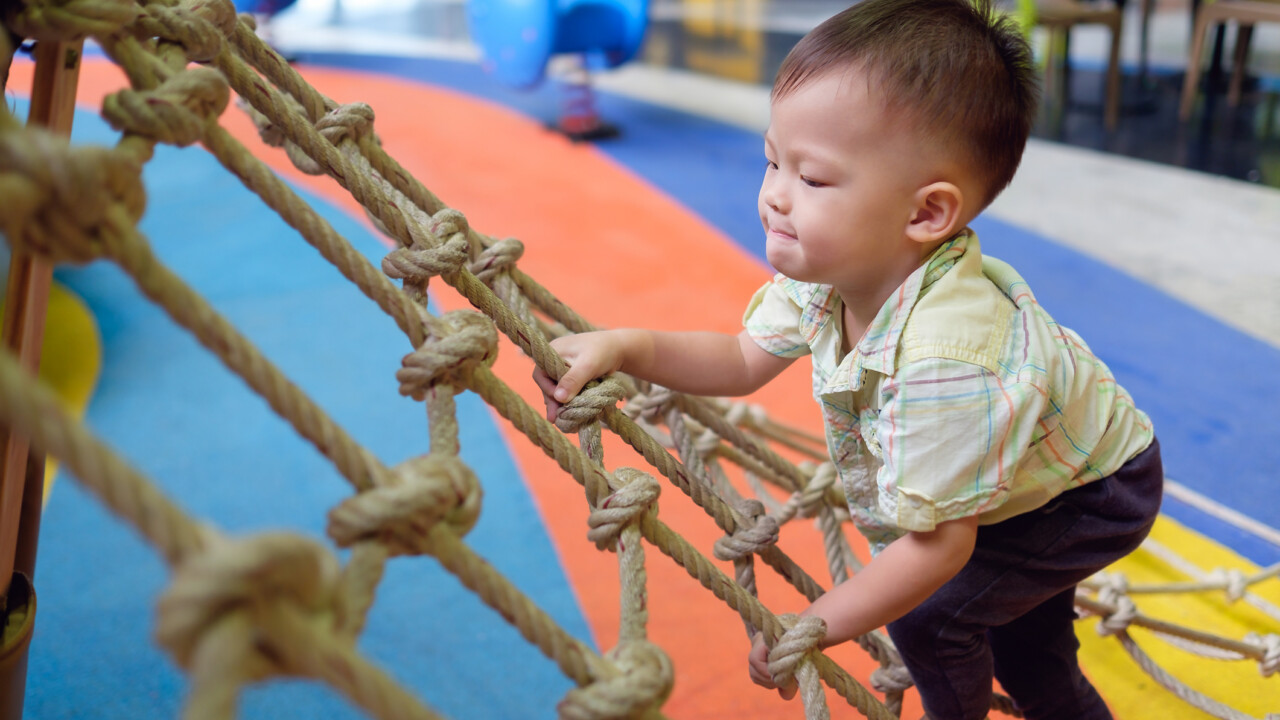 A young boy climbing on a rope in a playground.