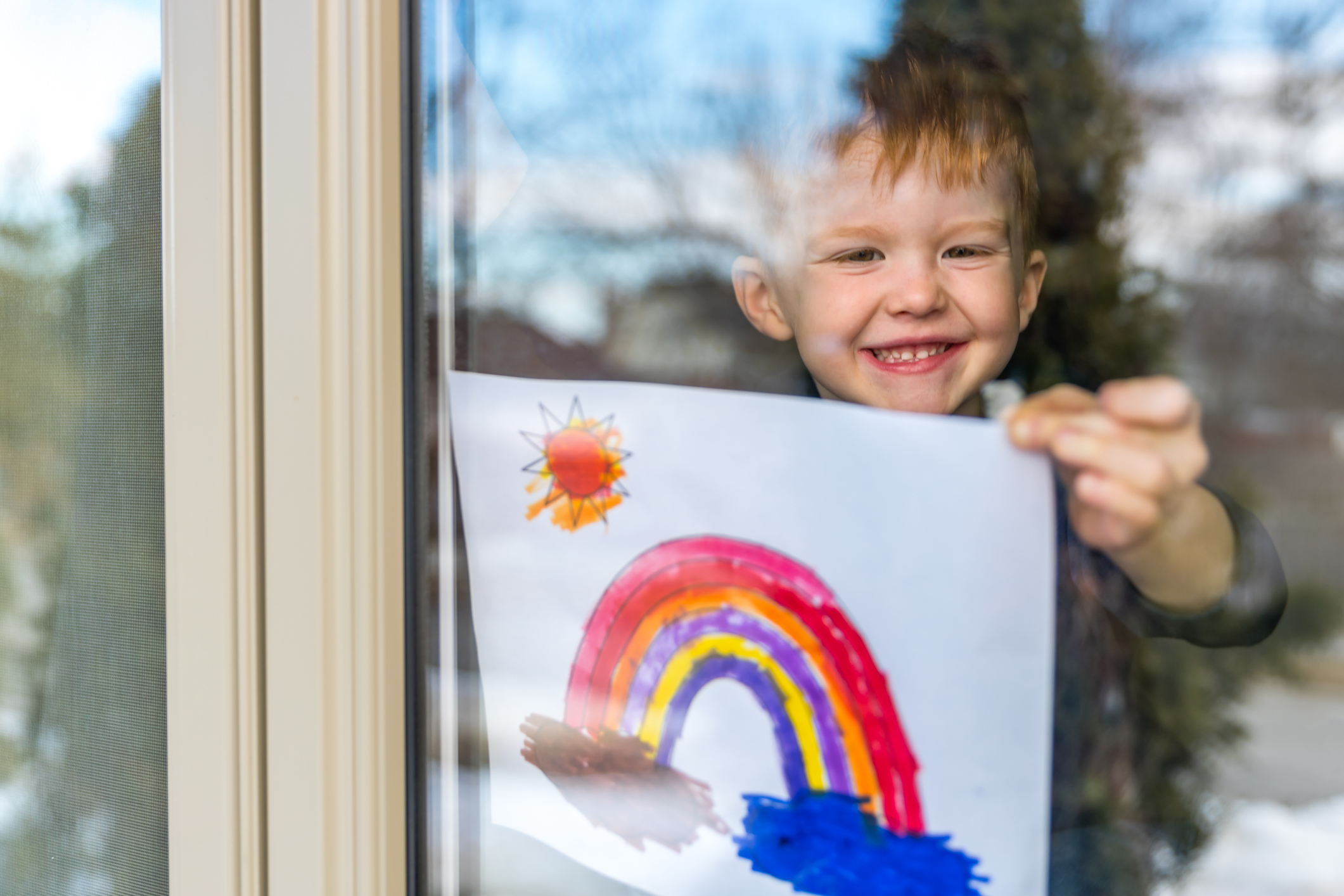 A young boy holding up a paper with a rainbow on it.